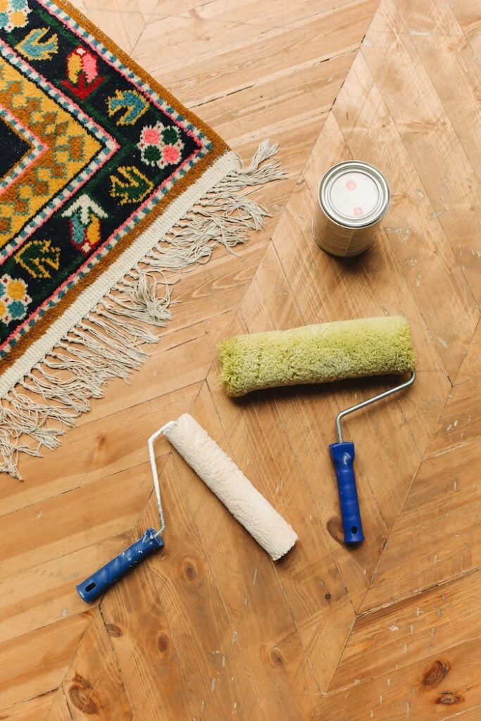 A decorative rug on wooden flooring with paint rollers and a can for home renovation.
